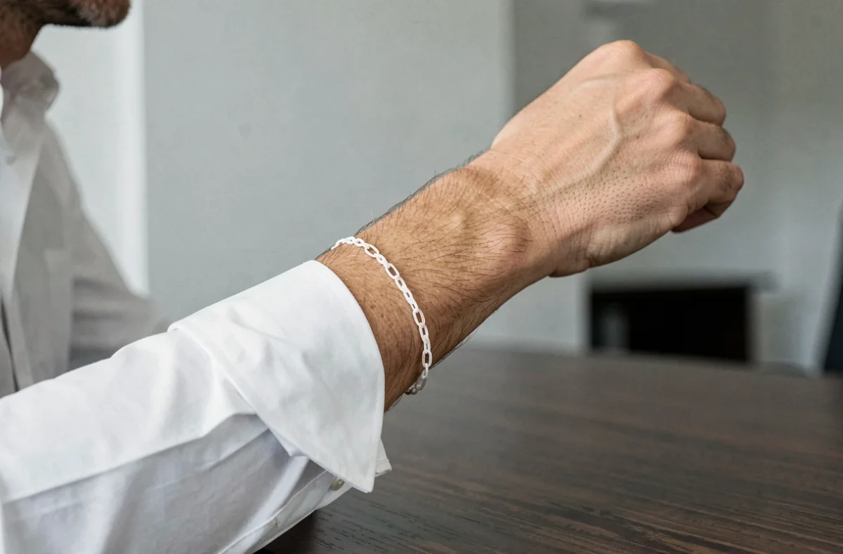 Homme élégant portant un bracelet en or blanc fin au poignet, tenue chemise blanche en environnement bureau moderne